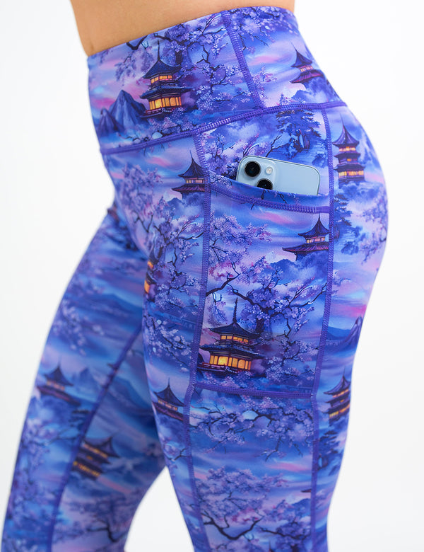 close up of the lavender and blue floral leggings featuring traditional pagodas and blooming cherry trees with a phone in its pocket