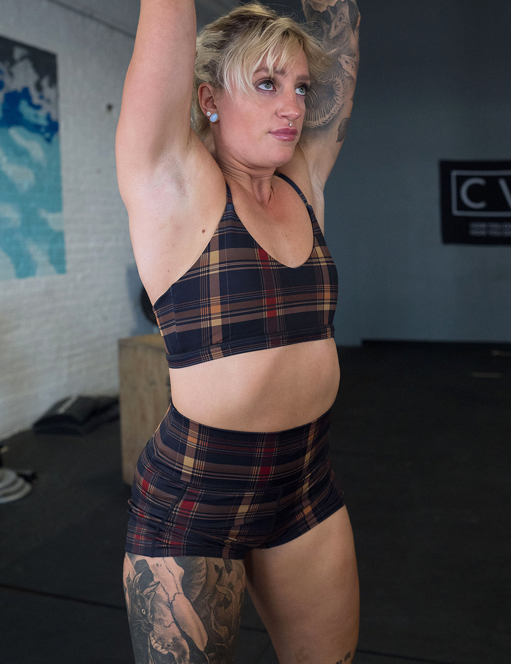 model wearing the 2.5 inch black, red, and gold plaid shorts and bra working out in the gym