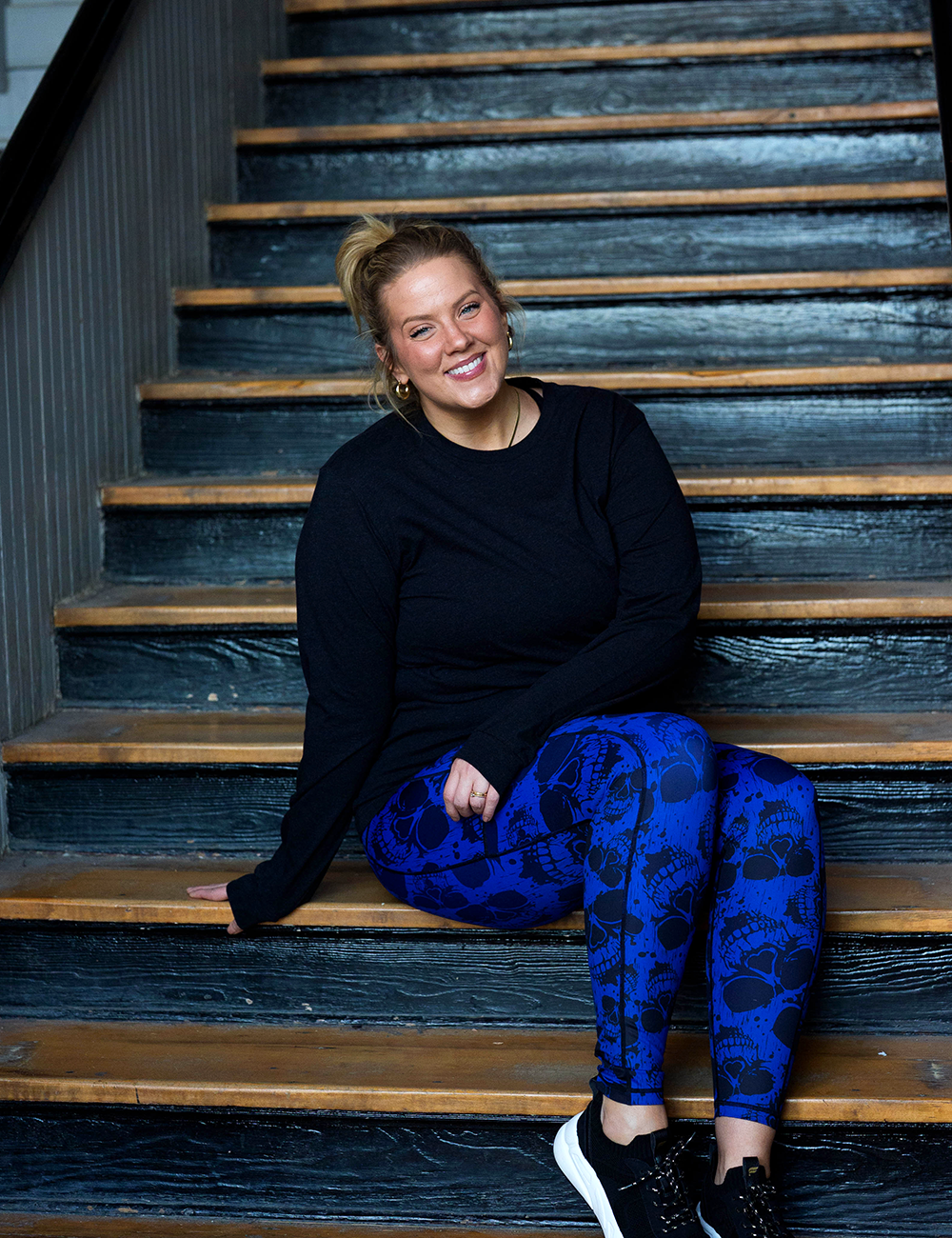 model wearing the dark skulls against a blue background pattern full length leggings sitting on the stairs