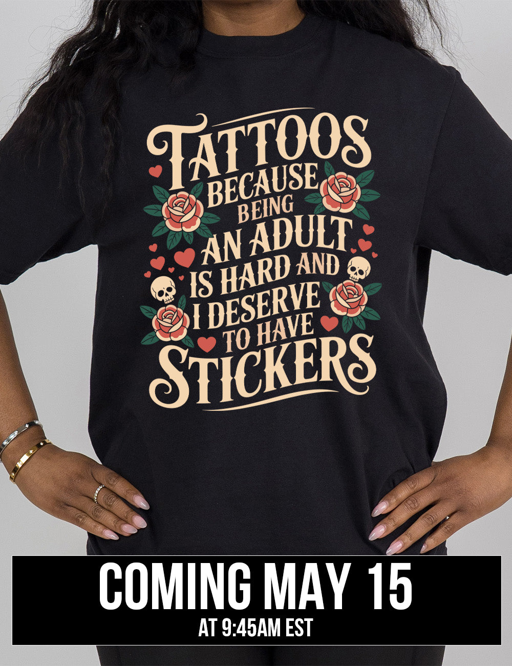 black modern tee with print placement on the front, with the words "tattoos because being an adult is hard and I deserve to have stickers" on it, with the graphics of roses, hearts, and skulls on the side of the words, coming may 15th