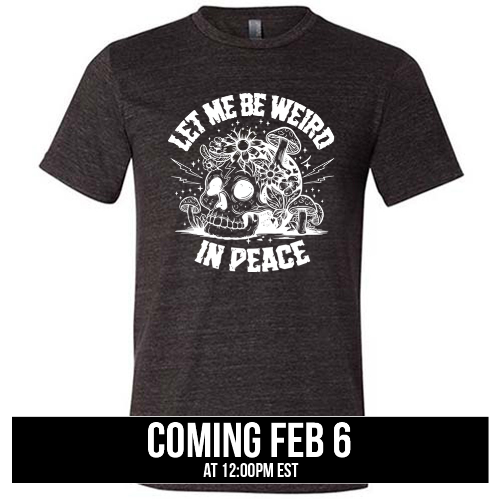 black unisex tee with the words "let me be weird in peace" on it with the graphic of a skull on the ground with mushrooms growing on and around it, as well as flowers growing on it, surrounded by little stars and lightening bolts, coming soon