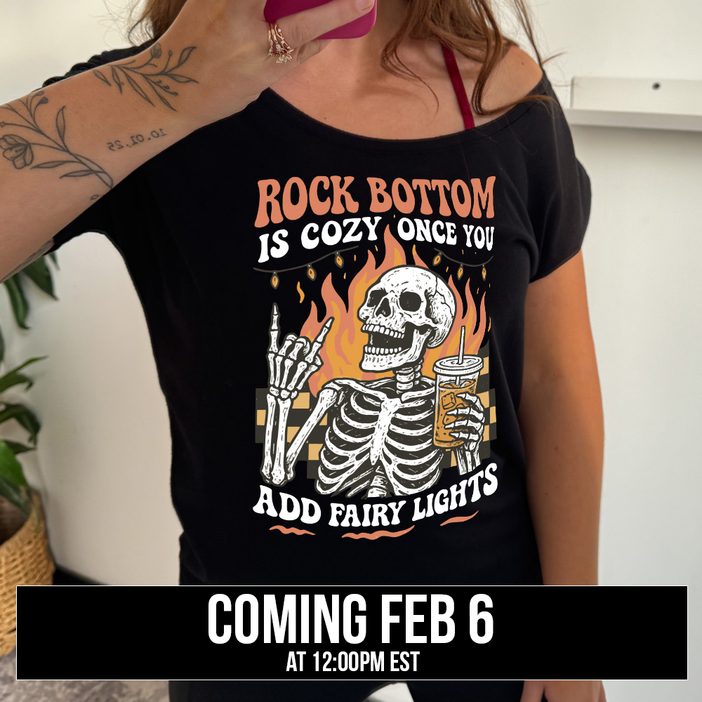 black unisex tee with the graphic of a rocker skeleton hand, surrounded by little stars as well as an archway of text saying "die with memories not dreams", coming soon