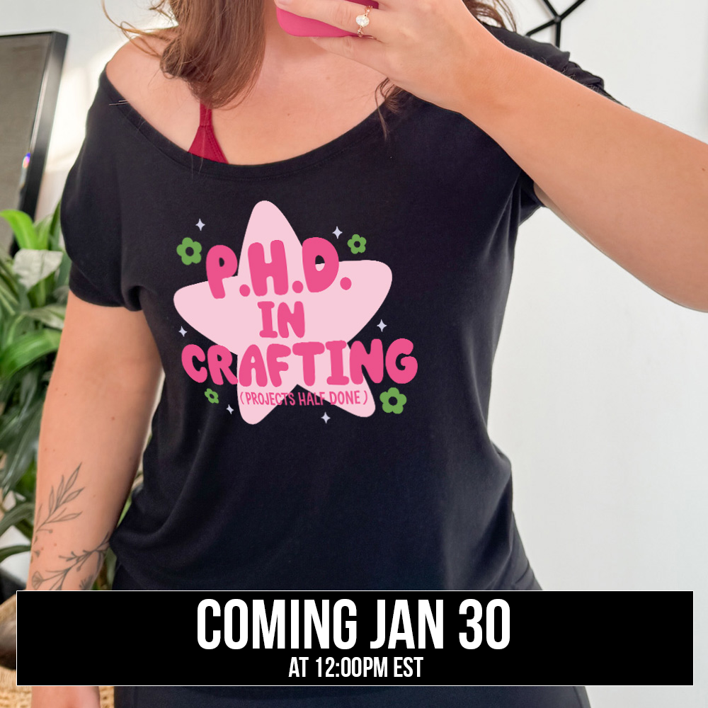 black slouchy tee with cartoon graphic of a large star behind the words "P.H.D.  in Crafting" in large font with the words (Projects Half Done) in small font underneath, with very small flowers and stars around, coming soon