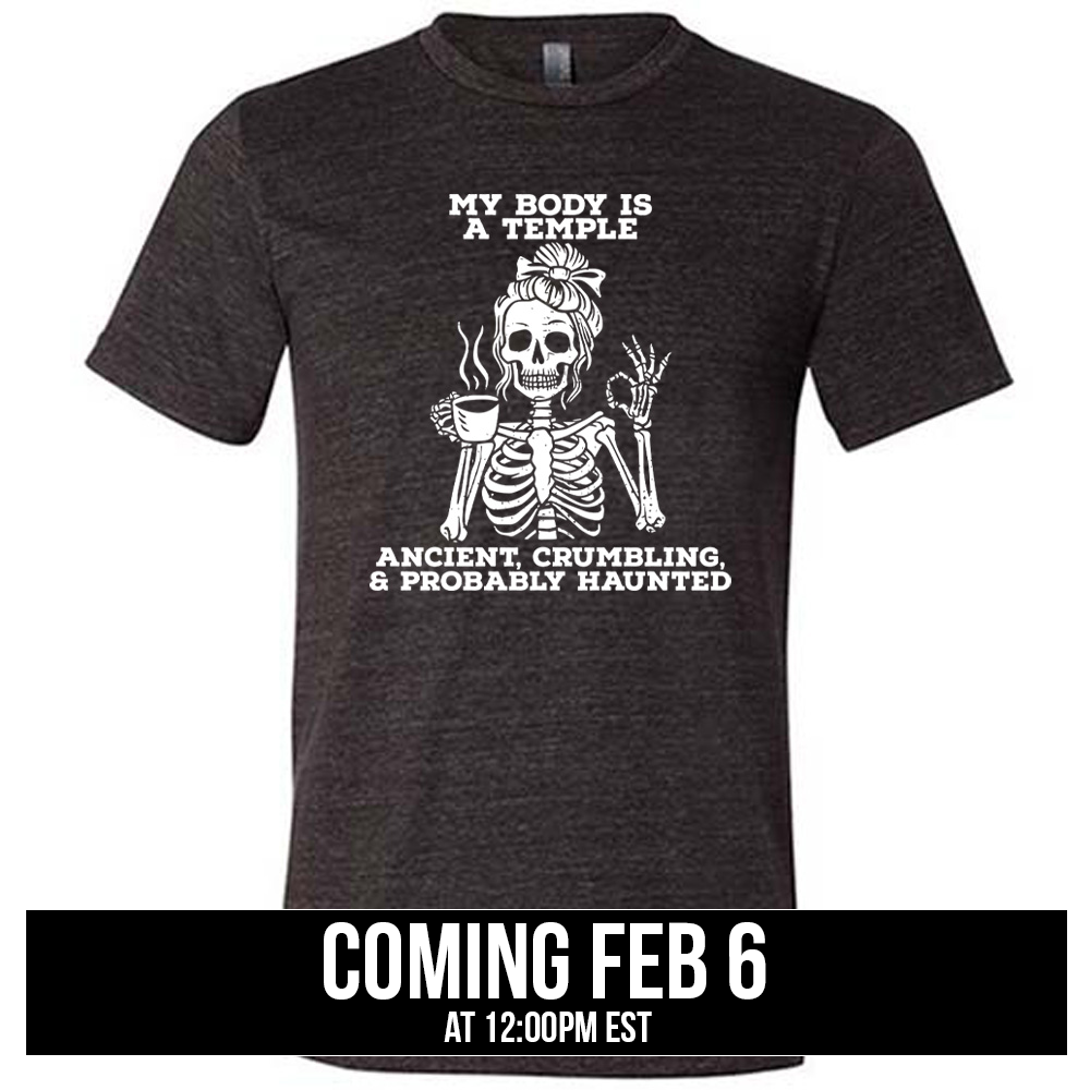 black unisex tee with the words "My Body Is a Temple Ancient, Crumbling, & Probably Haunted" on it, with the graphic of a skeleton with its hair in a bow, with one hand holding steaming coffee, and the other giving the OK symbol, coming soon
