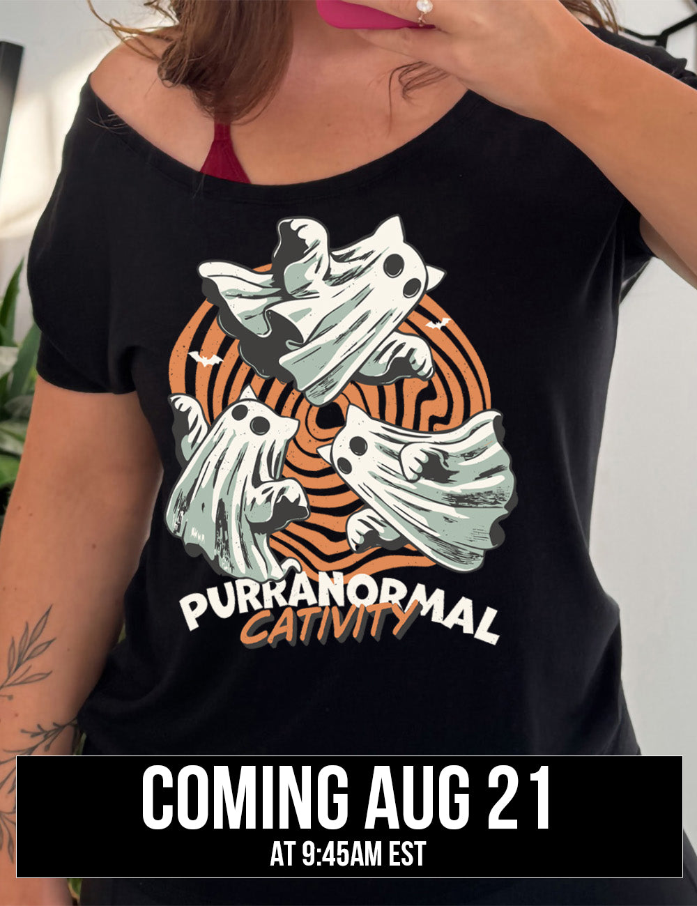 black slouchy tee with the graphic of three cat-ghosts swirling in a circle, in front of a spiraled background, with words underneath saying "purranormal cativity", coming august 21st