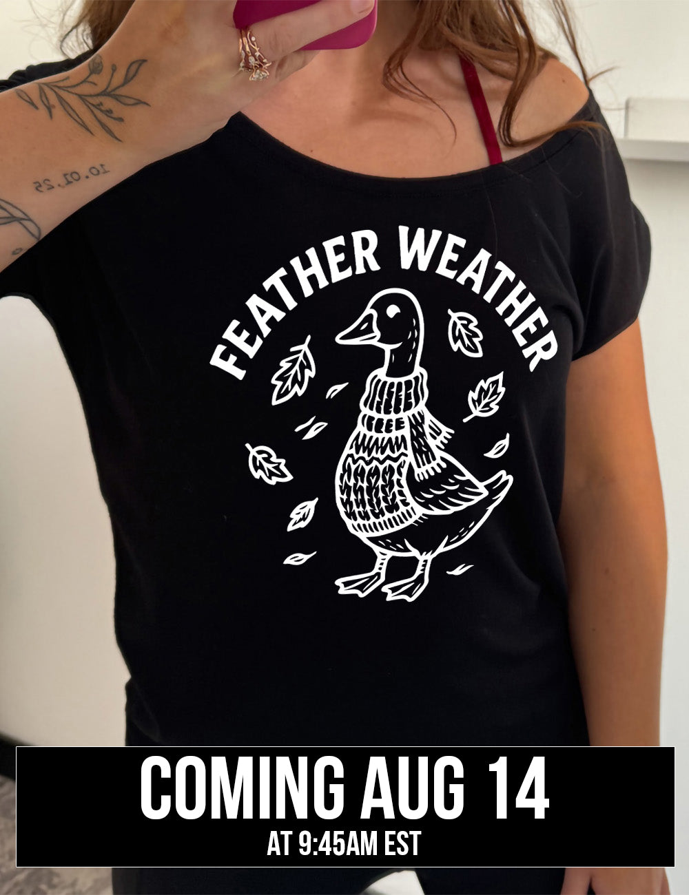 black slouchy tee with the graphic of a goose, wearing a scarf and sweater, surrounded by falling leaves, and the words arched over it saying "feather weather" coming august 14th
