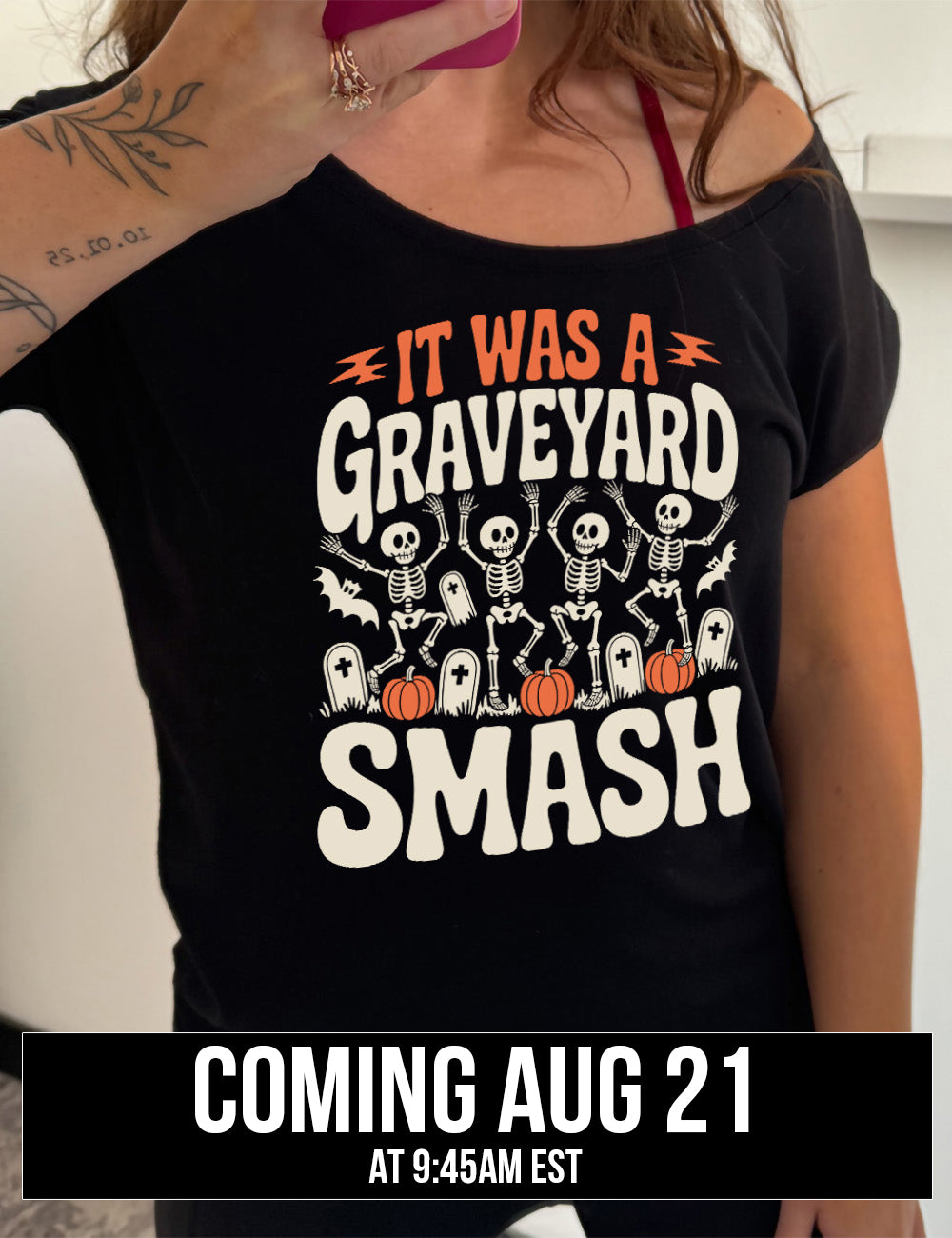 black slouchy tee with the words "it was a graveyard smash" with a lightning bolt on either side of the words "it was a" and the large graphic in the middle of the words of four skeletons dancing next to tombstones, pumpkins, and two bats, coming august 21st