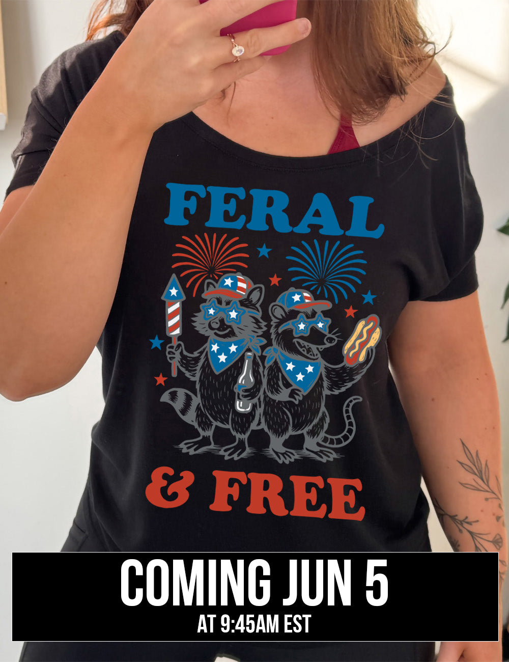 black slouchy tee with the words "feral & free" around the graphic of two racoons, both wearing American flag hats, sunglasses, and bandanas, one holding a firework and a beer bottle, the other holing a hotdogs, and fireworks going off above, and a few little stars, coming june 5th