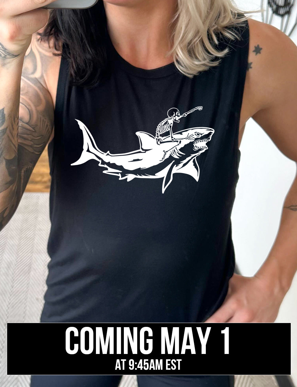 black muscle tank with the graphic of a skeleton, with its fist pointing onwards and its mouth open, riding a shark, who has a fierce expression, coming soon