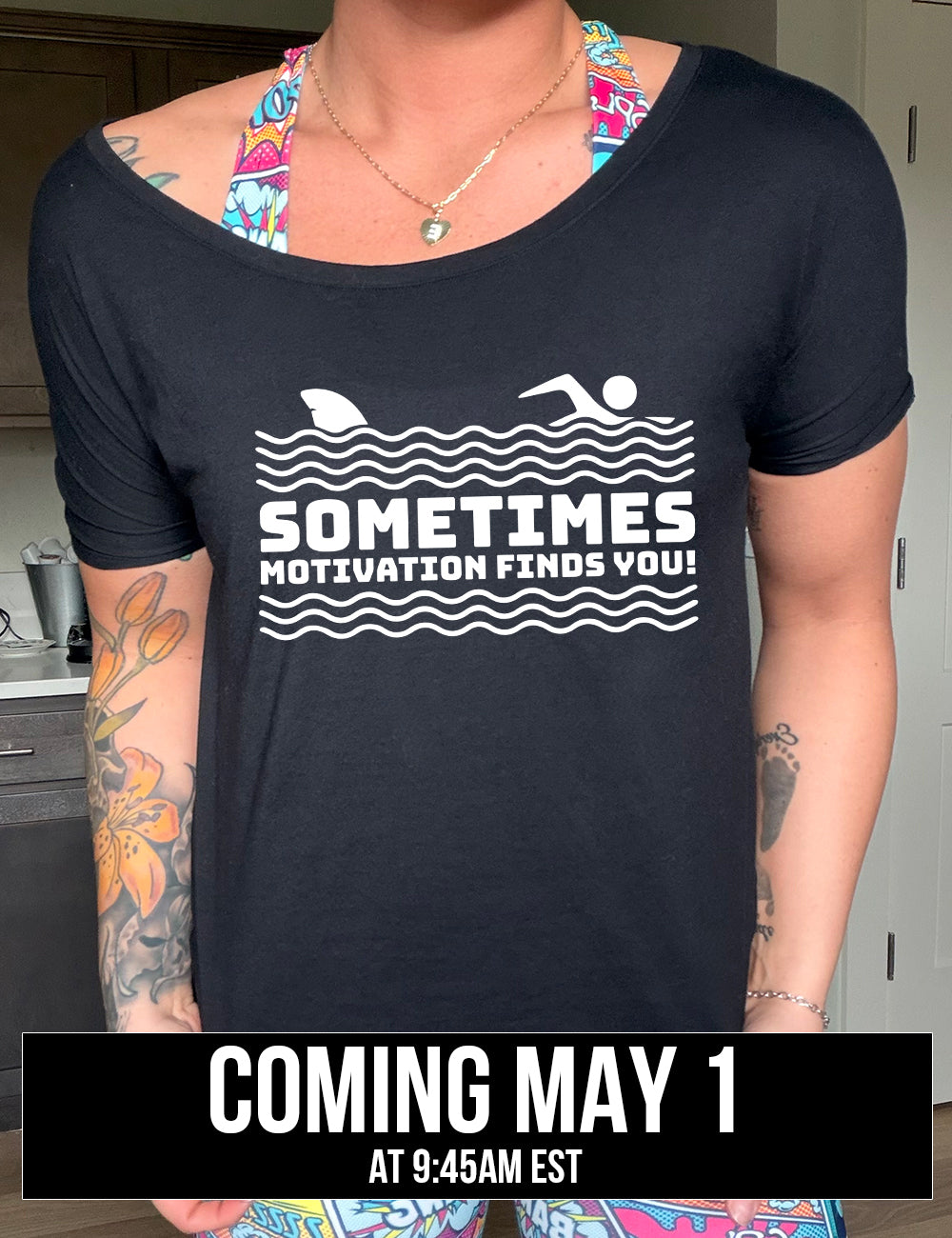 black slouchy tee with the words "sometimes motivation finds you!" in between the lined graphic of waves of the sea, and on top of the waves is the graphic of a figure swimming away from a fin in the water behind, coming soon