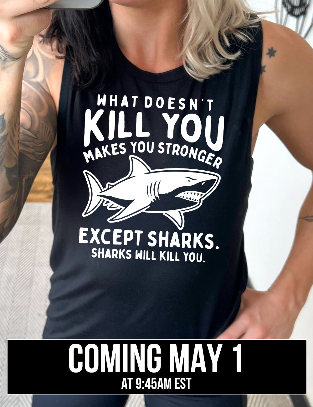 black muscle tank with the words "what doesn't kill you makes you stronger except sharks. sharks will kill you." and the graphic of a fierce shark in the middle, coming soon