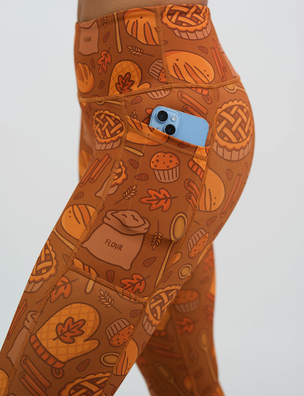 close up of the orange baking themed leggings with a phone in its pocket against a white background