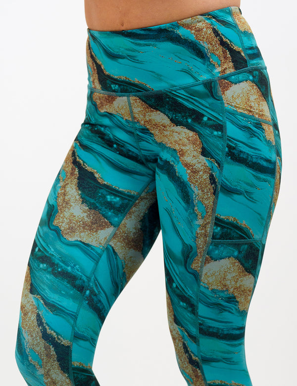 front of the blue ocean with gold streaks patterned leggings against a white background