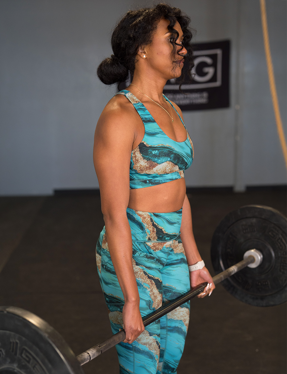 model in the gym wearing the crystal tides butterfly back bra and leggings while lifting weights