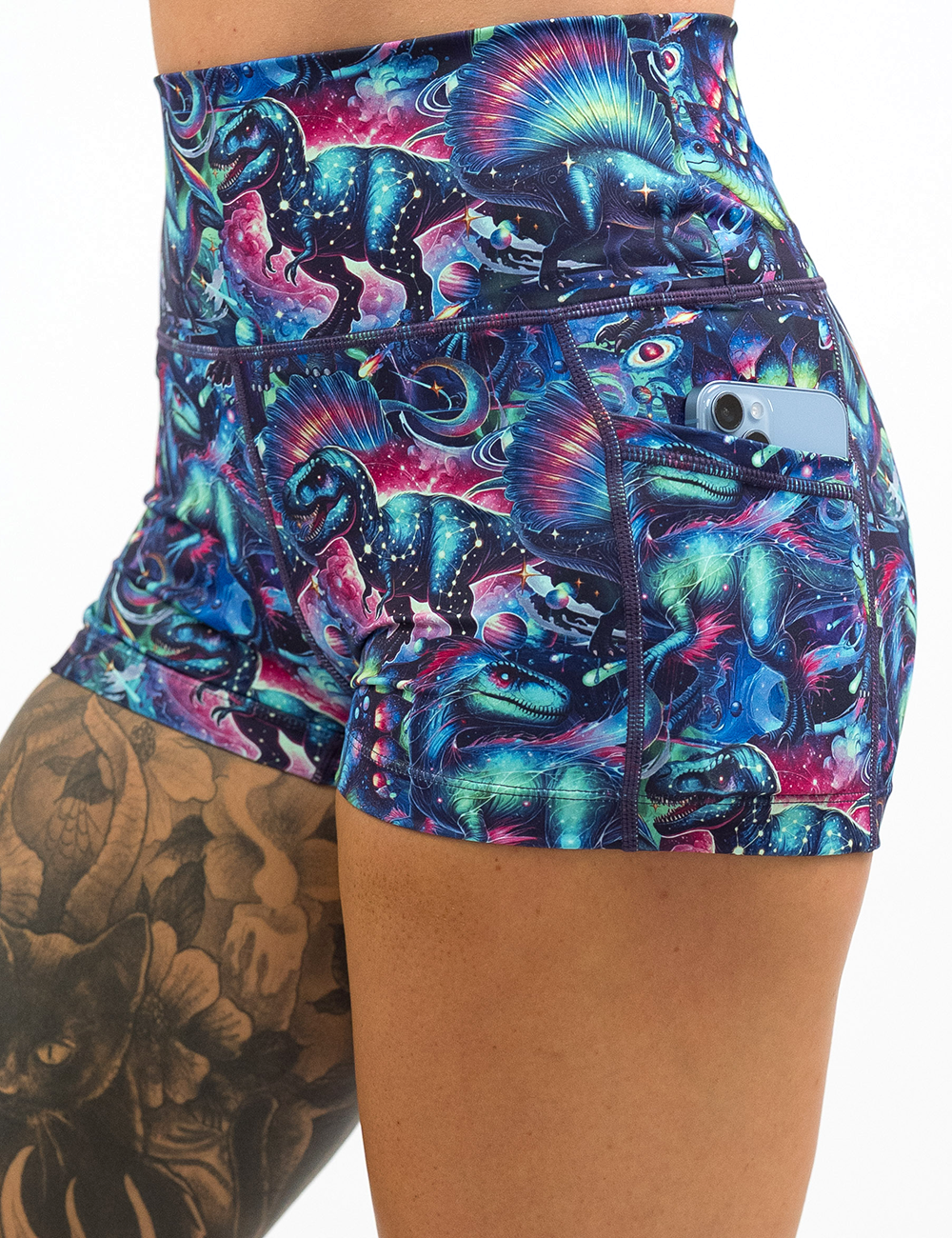 close up of the colorful dinosaur shorts with a phone in its pocket against a white background