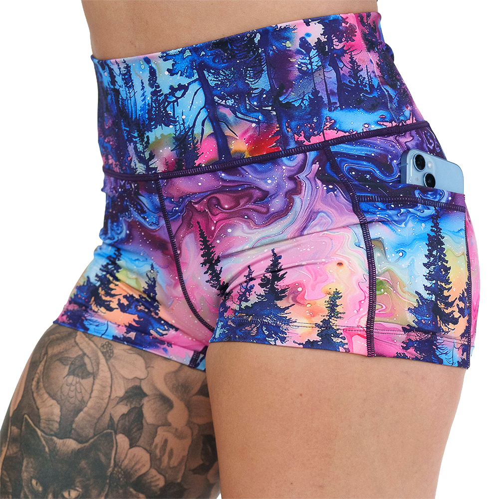 close up of the watercolor rainbow forest 2.5 inch shorts with a phone in the pocket against a white background