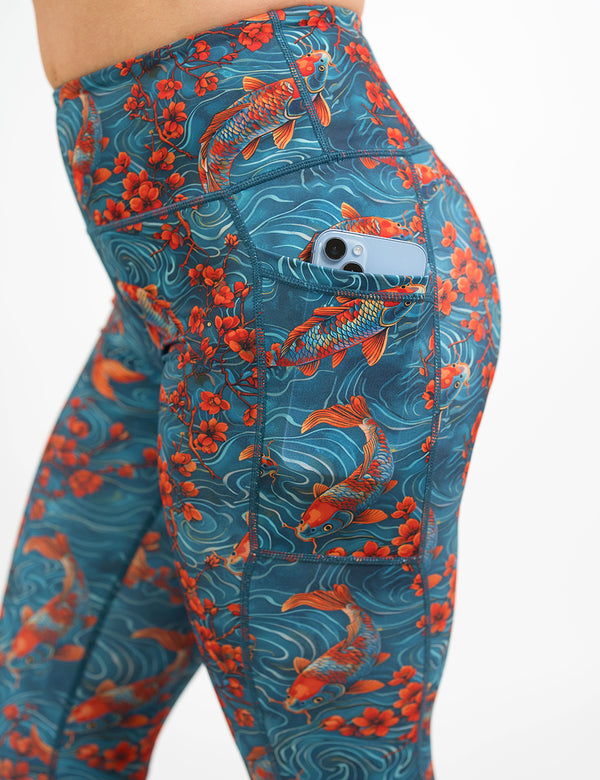 close up of the koi fish swimming with orange flowers pattern leggings with a phone in its pocket