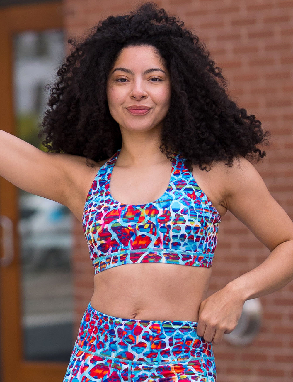 model wearing the yellow, orange, and blue mosaic style butterfly back bra against a brick background