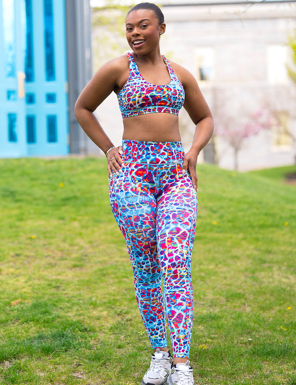 model wearing the turquoise, coral, pink, orange, purple, and yellow mosaic style pattern full length leggings and bra in the park