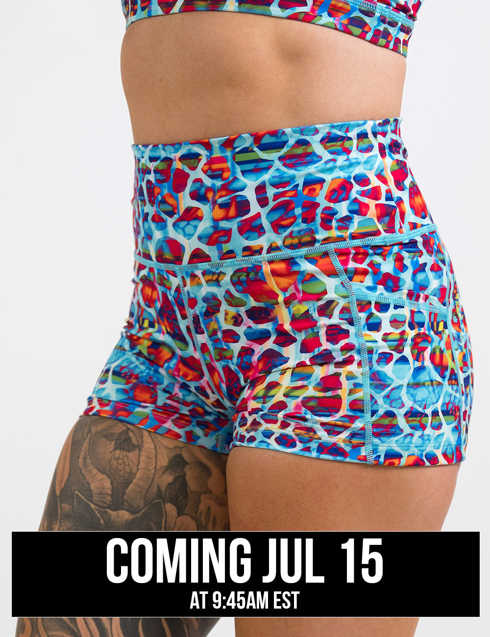 front of the 2.5 inch blue, red, teal, and yellow mosaic style shorts against a white background, coming july 15th