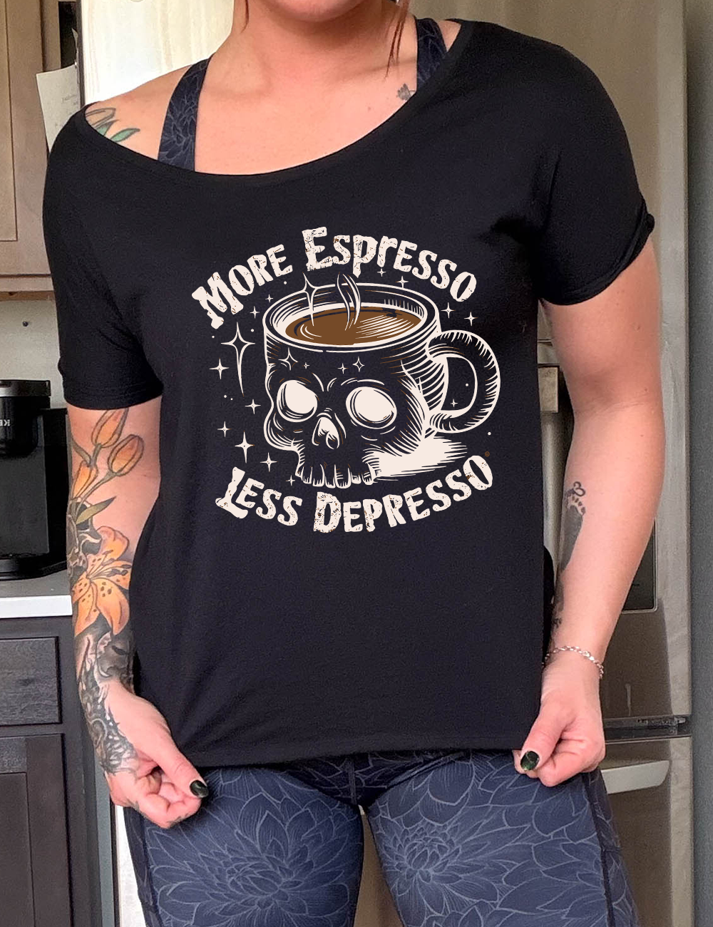 black slouchy tee with the words "more espresso less depresso on it, around the graphic of a skull-shaped mug full of a steaming beverage, with lots of little stars around