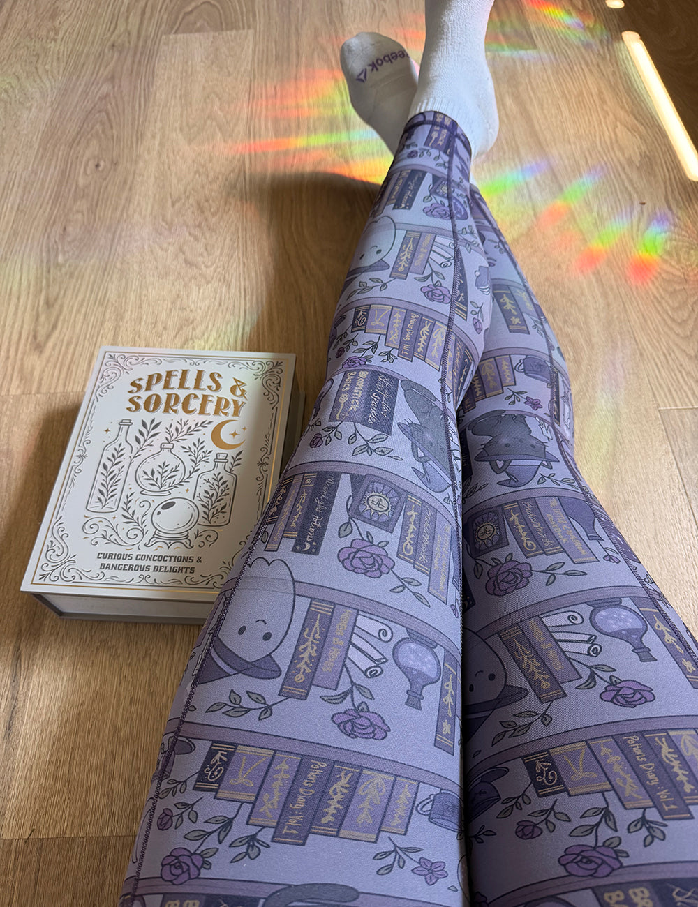 model wearing the front of the ghosts and cats book shelves full length leggings sitting next to a book titled "spells & sorcery"