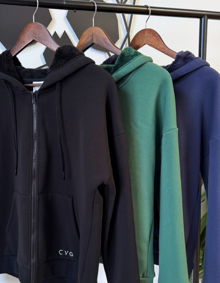 Three hoodies in black, green, and blue hanging on a rack.