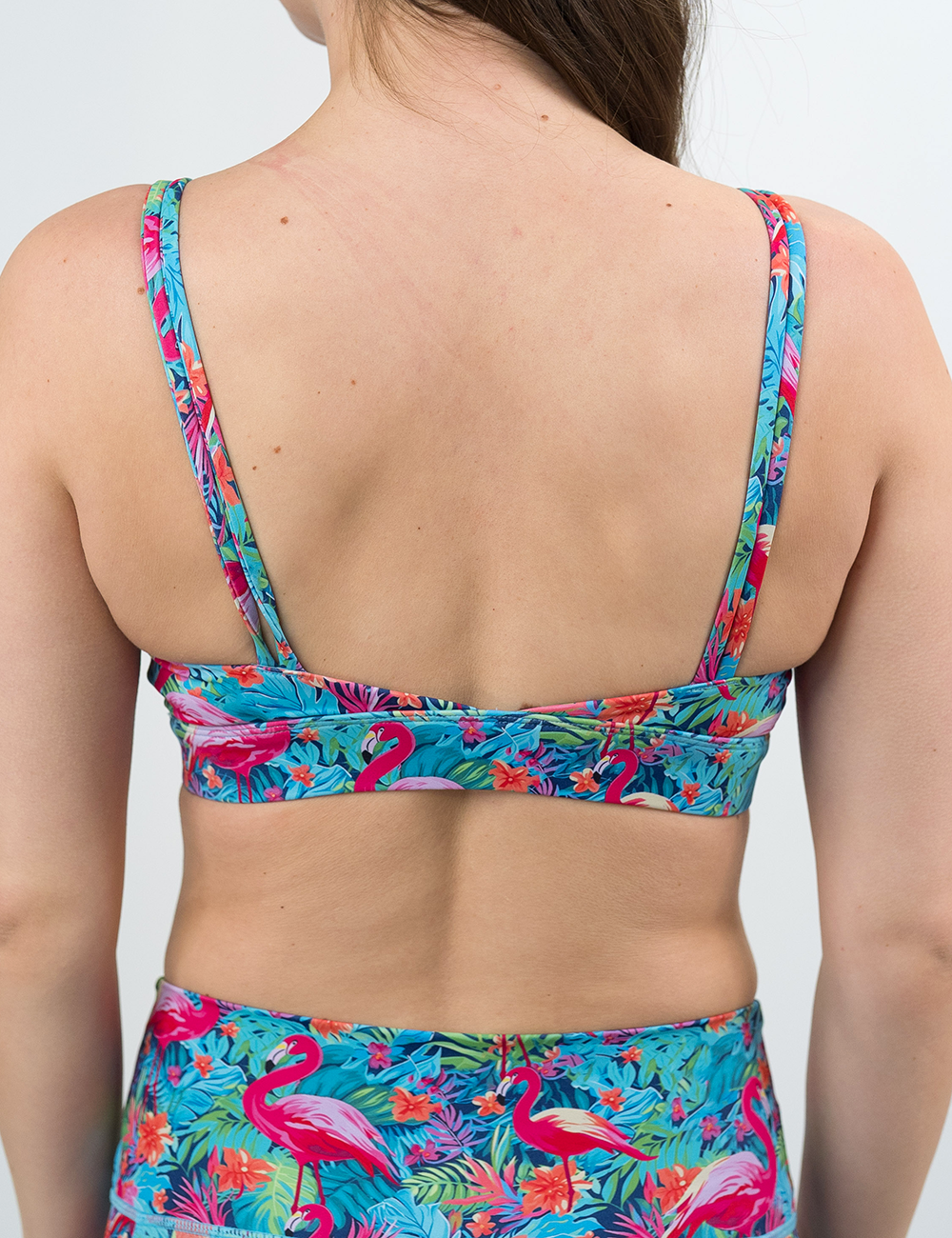 back of the flamingos against a colorful floral background patterned vitality bra against a white background