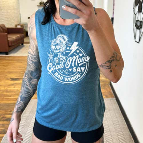 model wearing a deep teal muscle tank with the saying "good moms say bad words" and a female skeleton rock symbol hand and lightning bolt