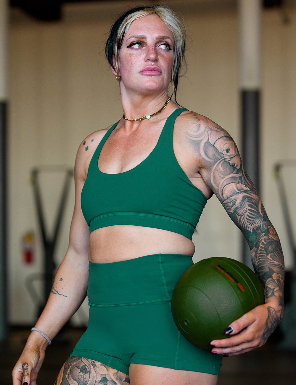 model wearing the solid green sports bra and shorts in the gym holding a medicine ball