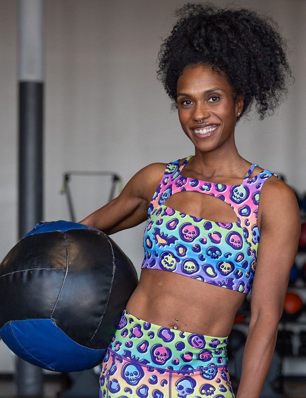 model wearing the rainbow leopard print pumpkins and skulls bra in the gym holding a medicine ball