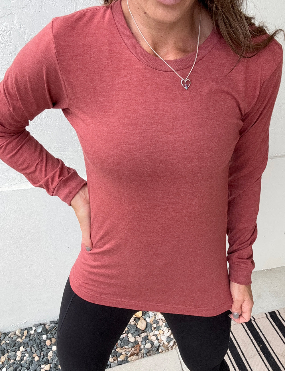 Person wearing a heather clay red long-sleeve shirt against a white wall
