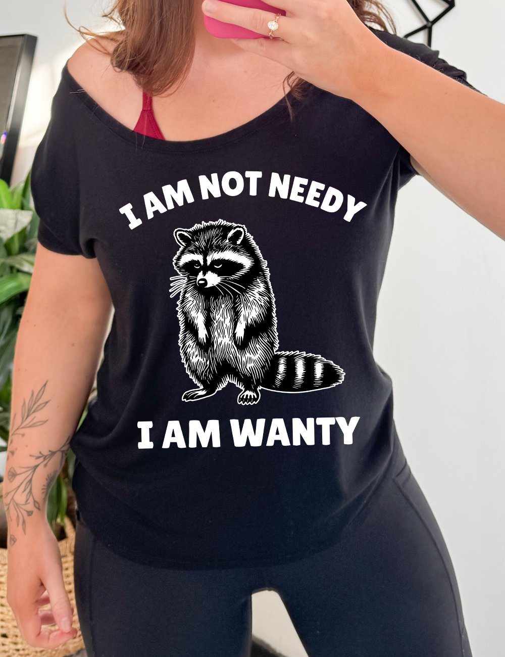 black slouchy tee with the graphic of a raccoon, hanging its head and drooping its arms, and the words "I am not needy I am wanty" on it