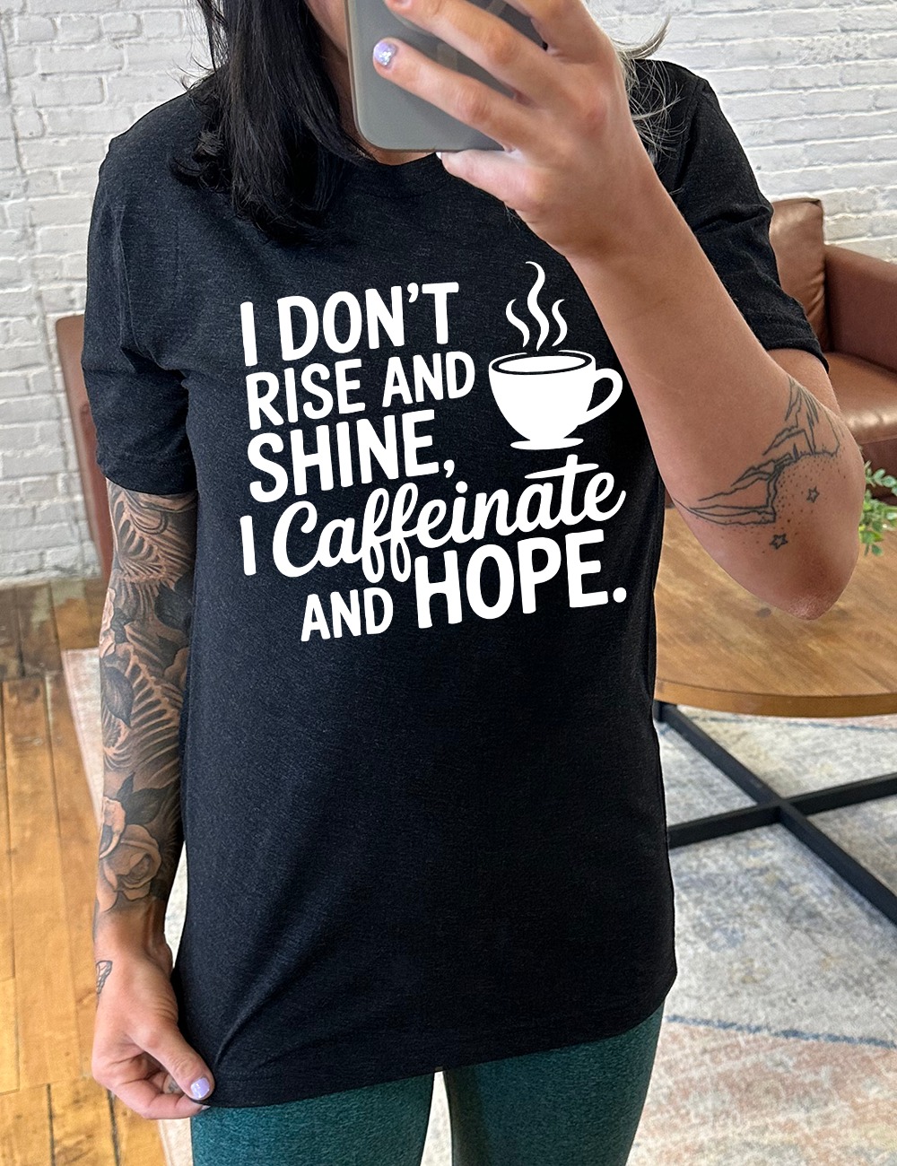 black unisex tee with the words "I don't rise and shine, I caffeinate and HOPE." on it, with the graphic of a steaming cup of a coffee