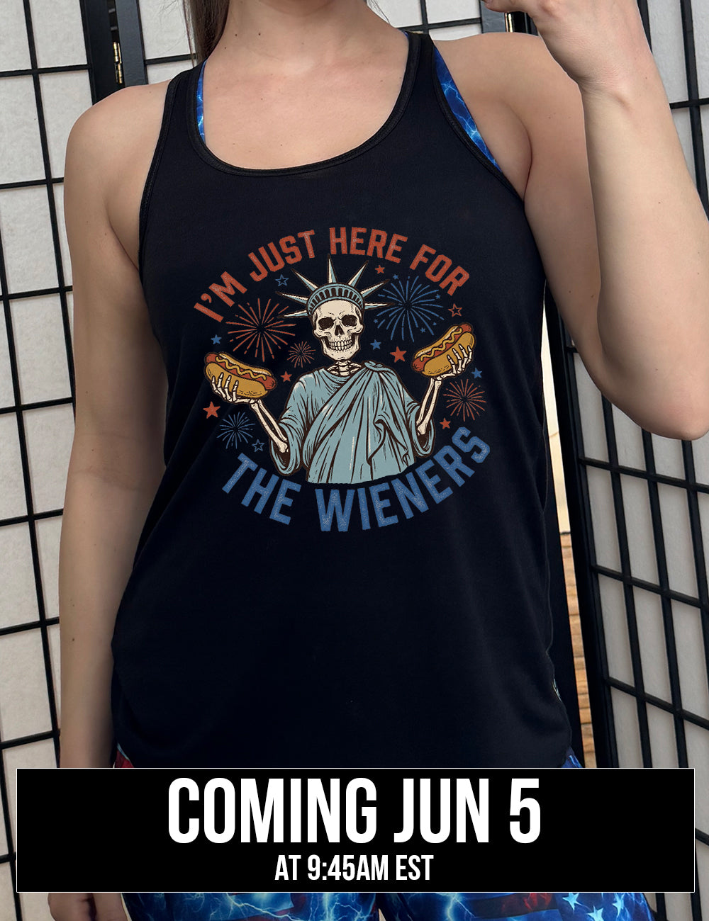 black flowy racerback tank with the words "I'm just here for the wieners" on it, with the graphic in the middle of the words of a skeletal statue of liberty with a hotdog in each hand and fireworks and stars around it, coming june 5th
