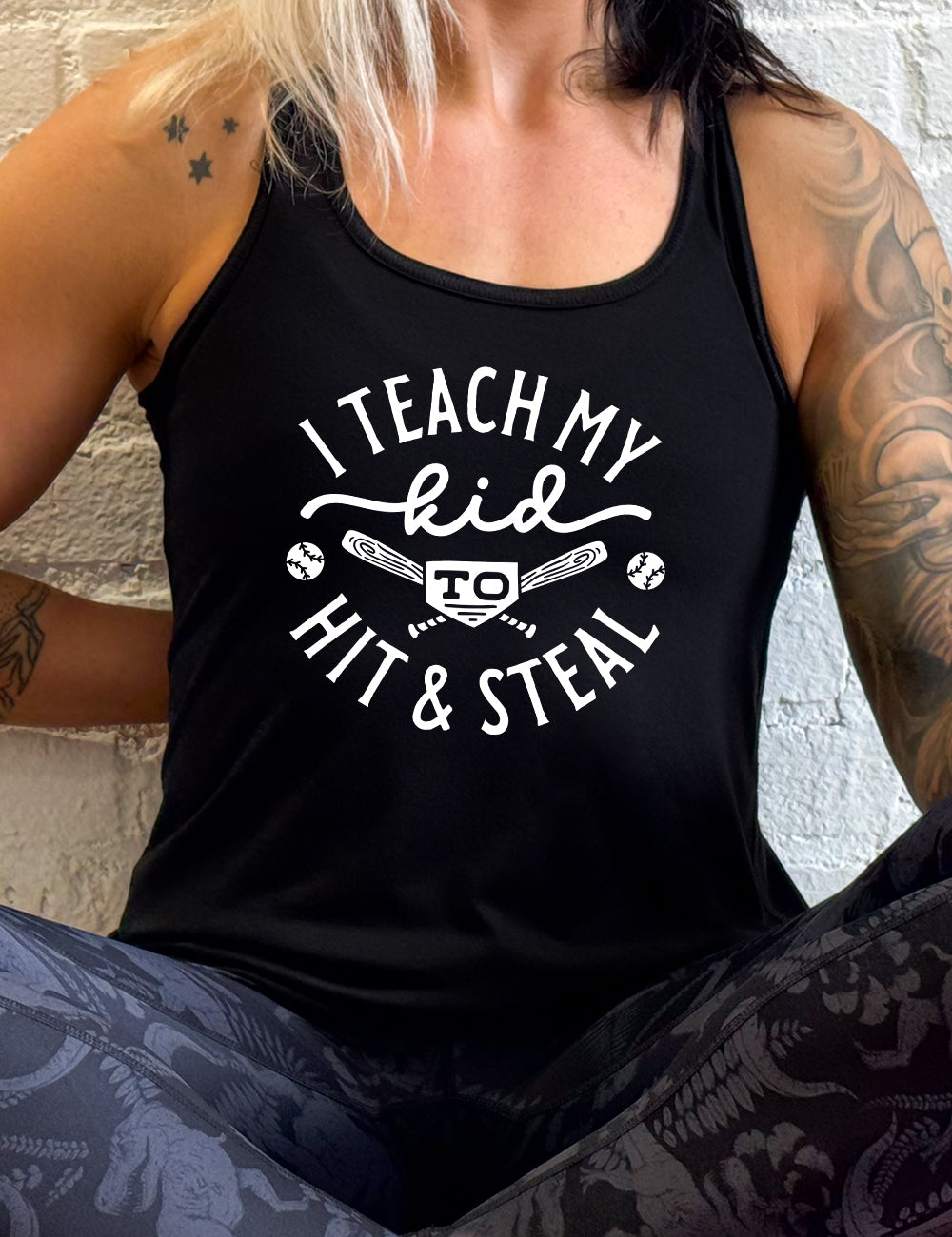 black flowy racerback tank with words saying "I teach my kid to hit & steal" on it, with two bats crossed behind the word "to", and a baseball on either side of that