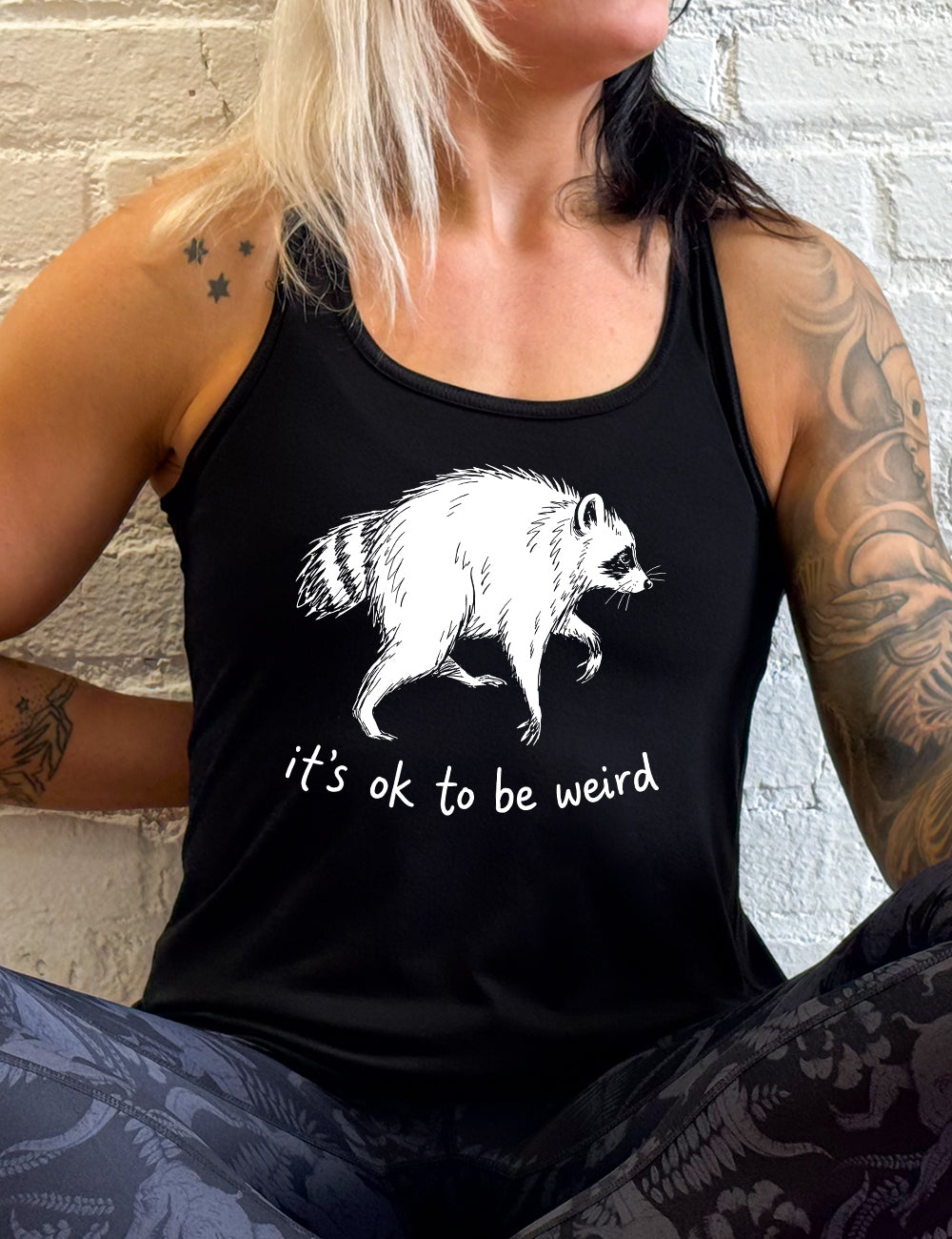 front of the black "it's ok to be weird" raccoon racerback tank
