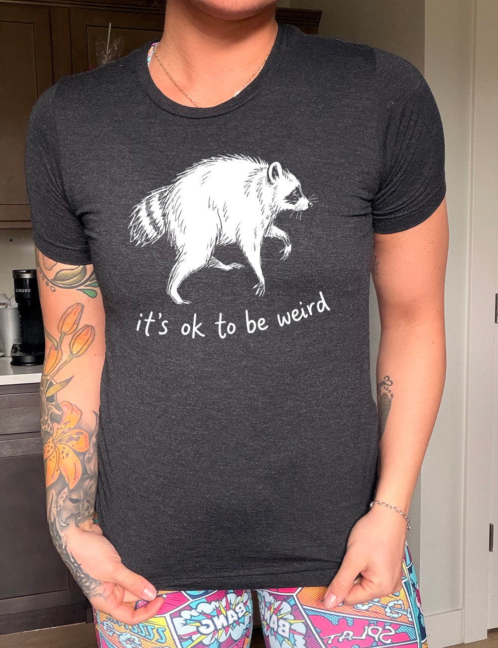 front of the black "it's okay to be weird" raccoon unisex tee