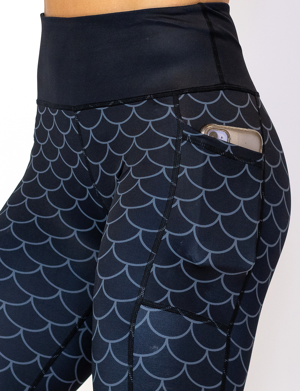 close up of the dragon scale outline against a dark background pattern leggings to show the pocket which has a phone in it