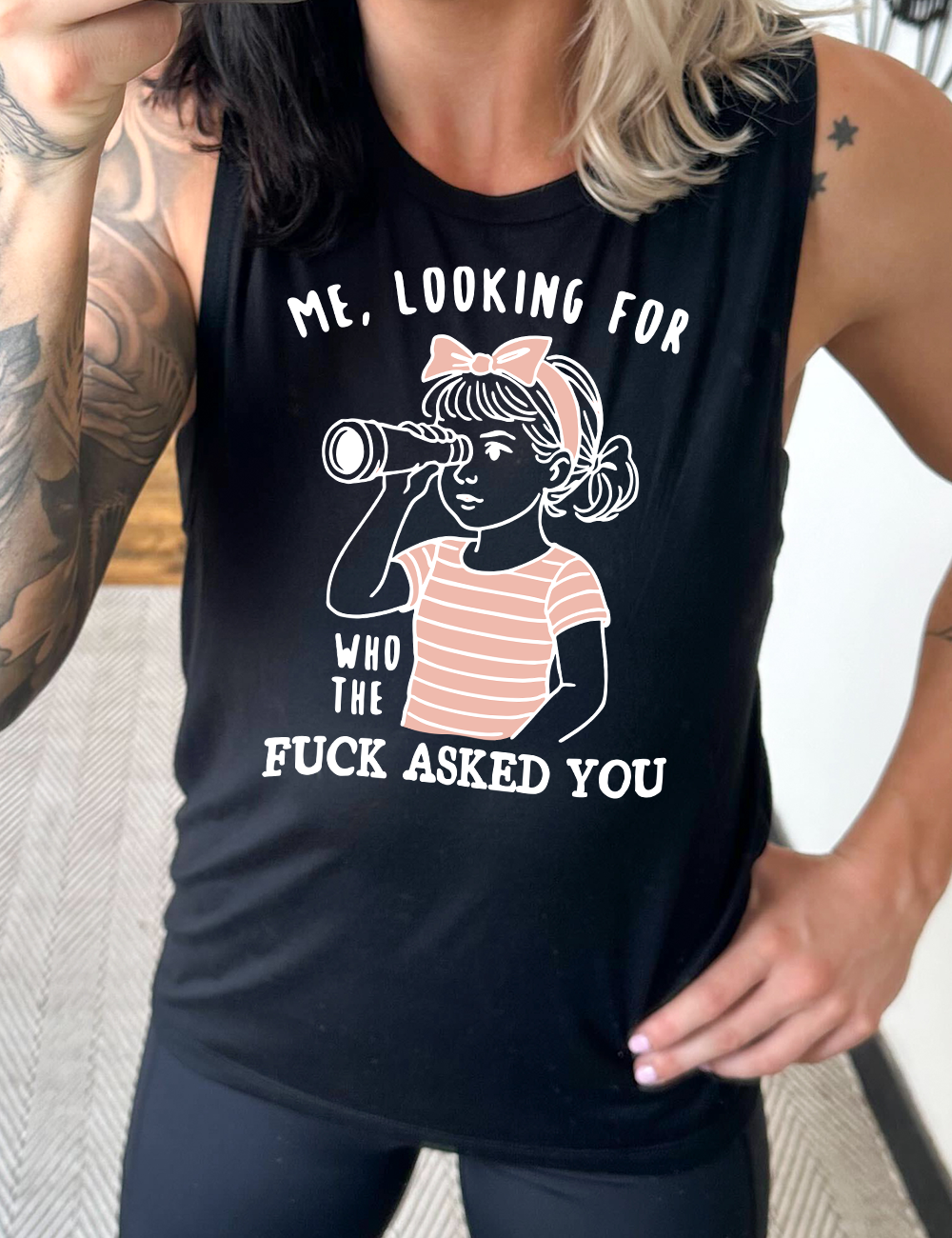 black muscle tank with the graphic of a young girl, wearing a striped pink shirt and a pink bowed headband and looking through a telescope, and the words "me, looking for who the fuck asked you" on it