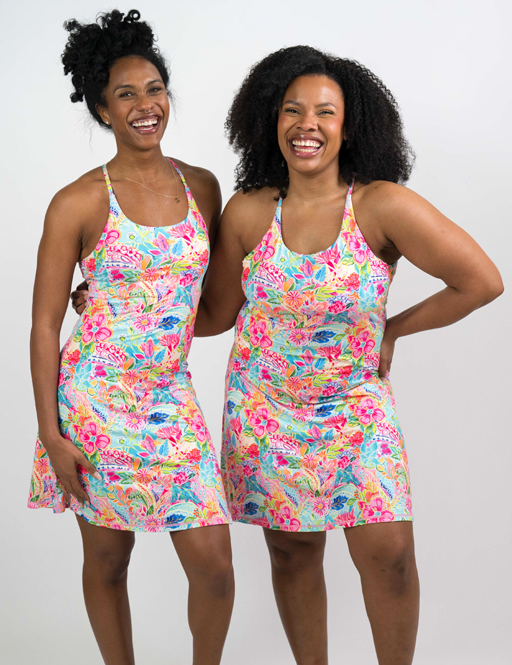 Two women wearing colorful floral dresses against a white background