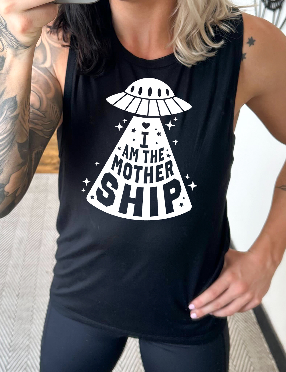 black muscle tank with the words "I am the mothership" on it within the beam of a UFO, with a heart above the words, and a number of stars scattered around