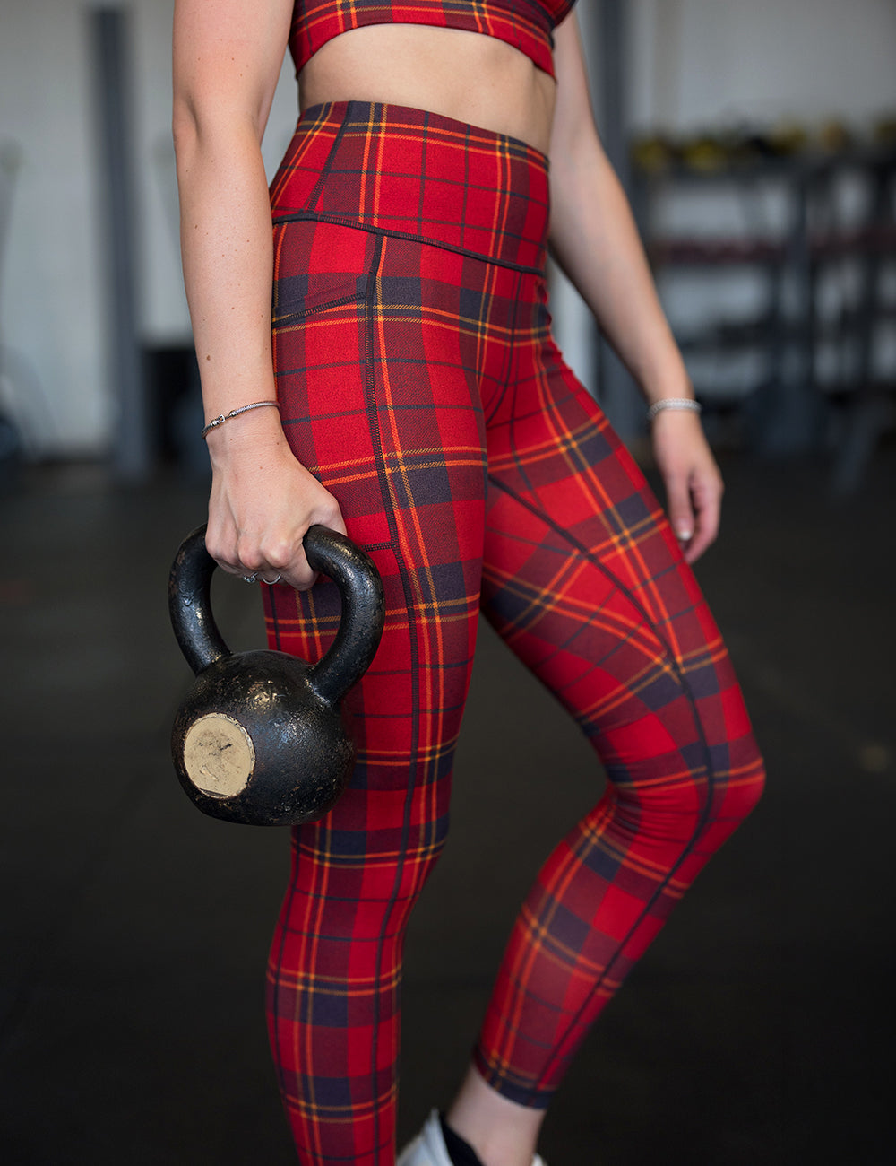 model wearing the full length red, yellow, and dark grey plaid leggings and bra working out in the gym