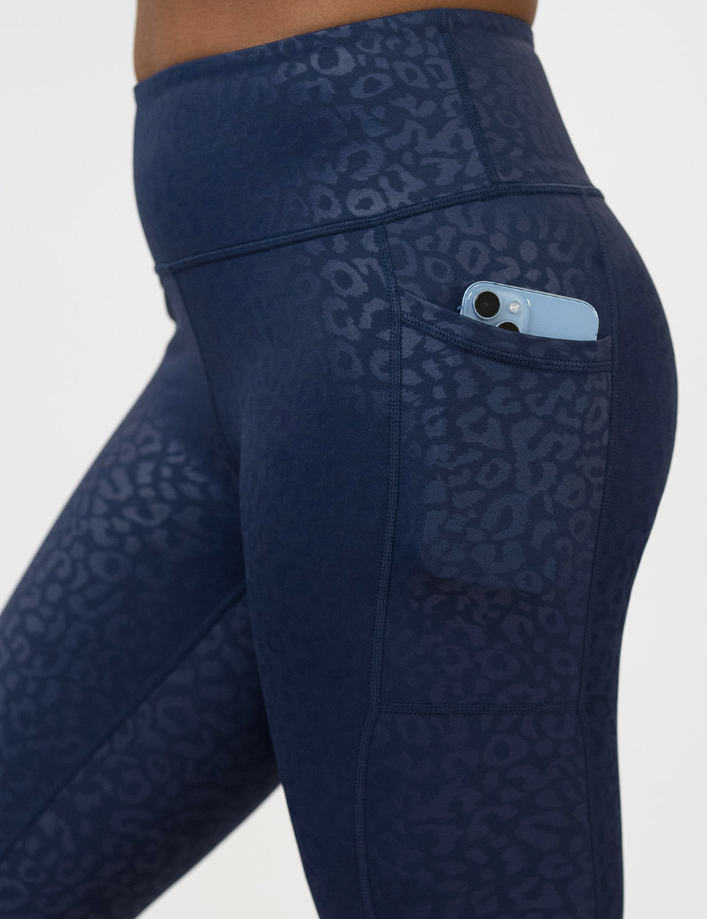 close up of the dark blue leopard print leggings with a phone in its pocket against a white background
