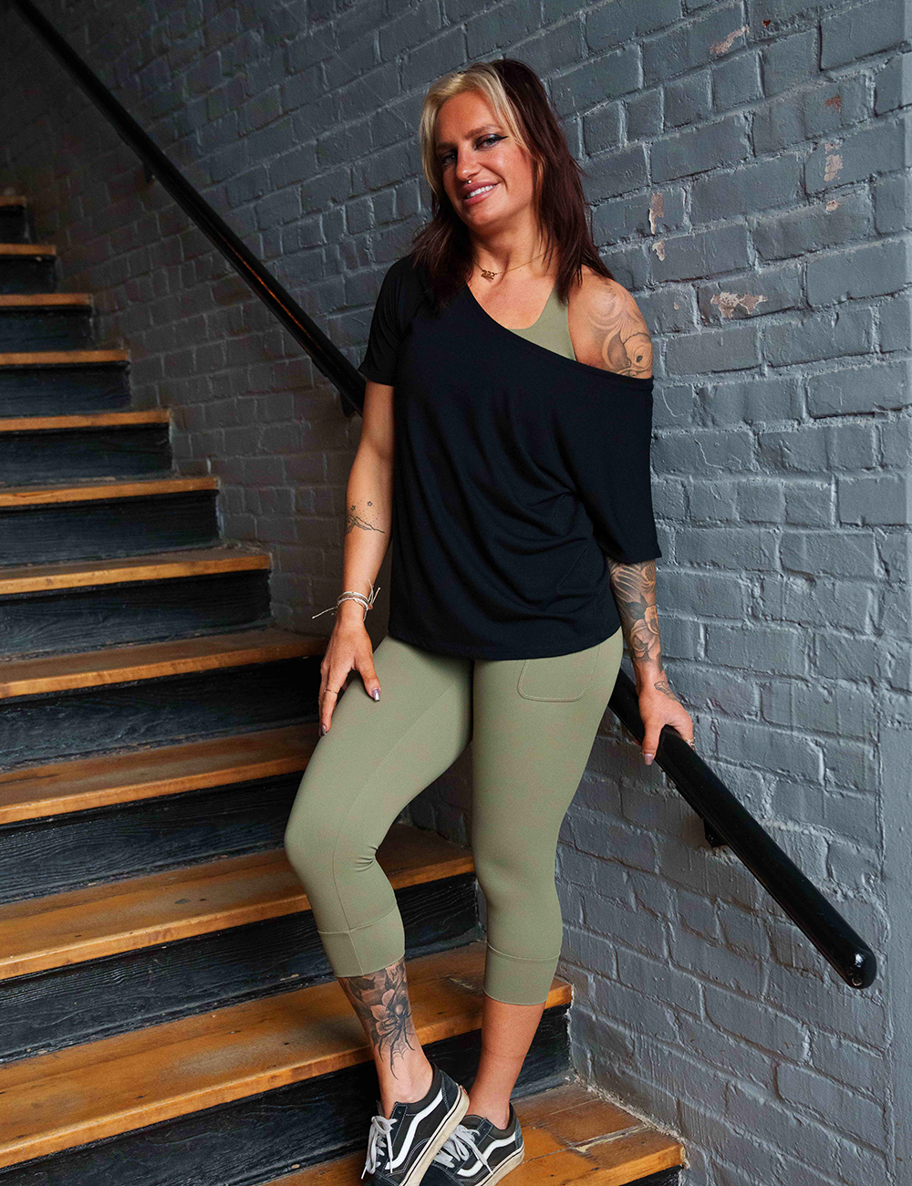 model wearing omni green tea leggings against a white brick background