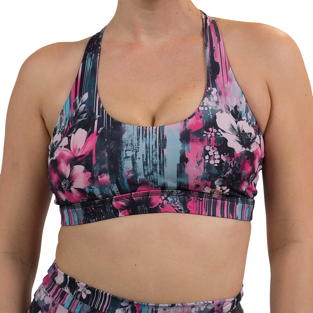 front of the pink flowers against a bold teal and pink striped background pattern butterfly back bra against a white background
