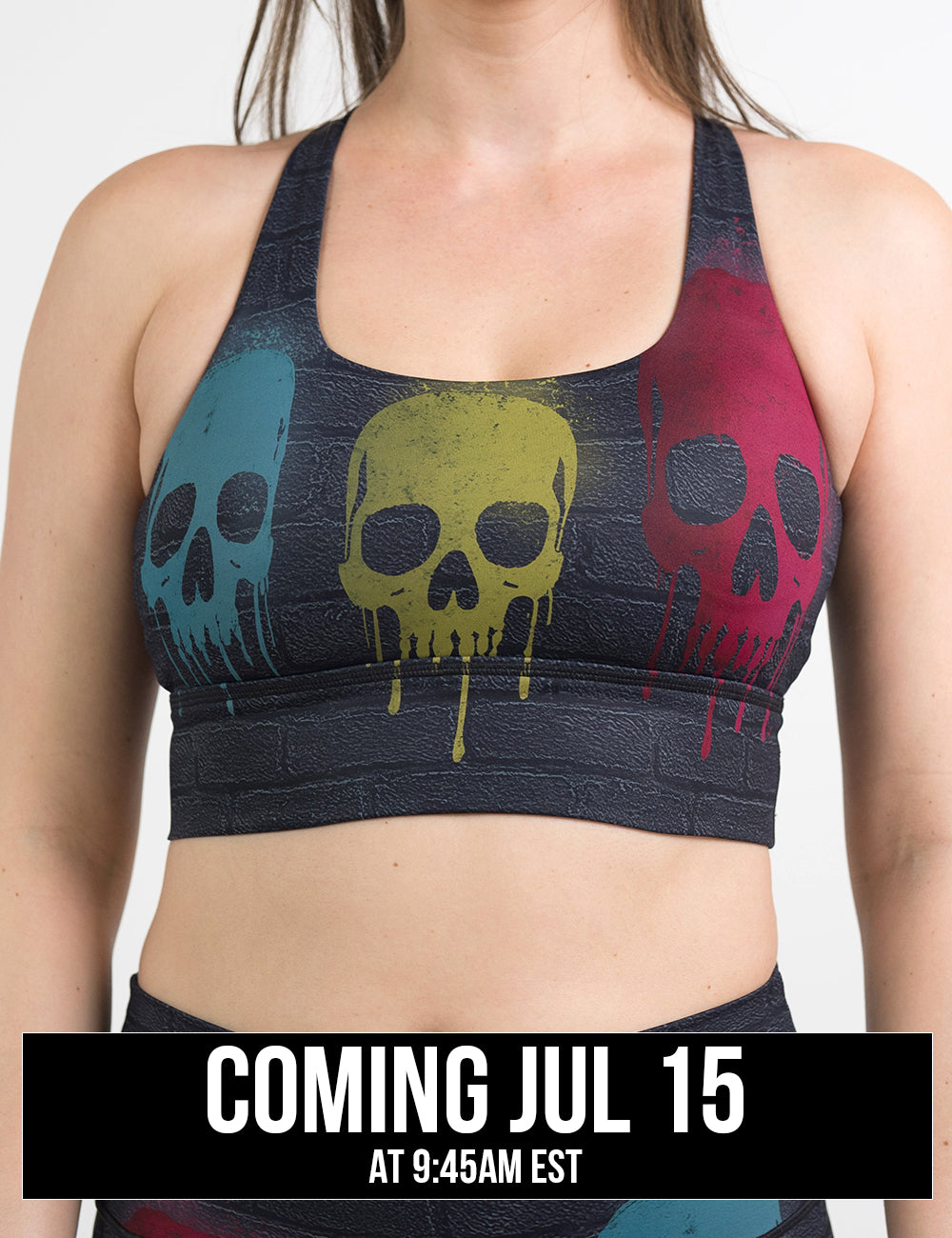 front of the black brick style longline bra with yellow, teal, and red skulls spray painted all over against a white background, coming july 15th