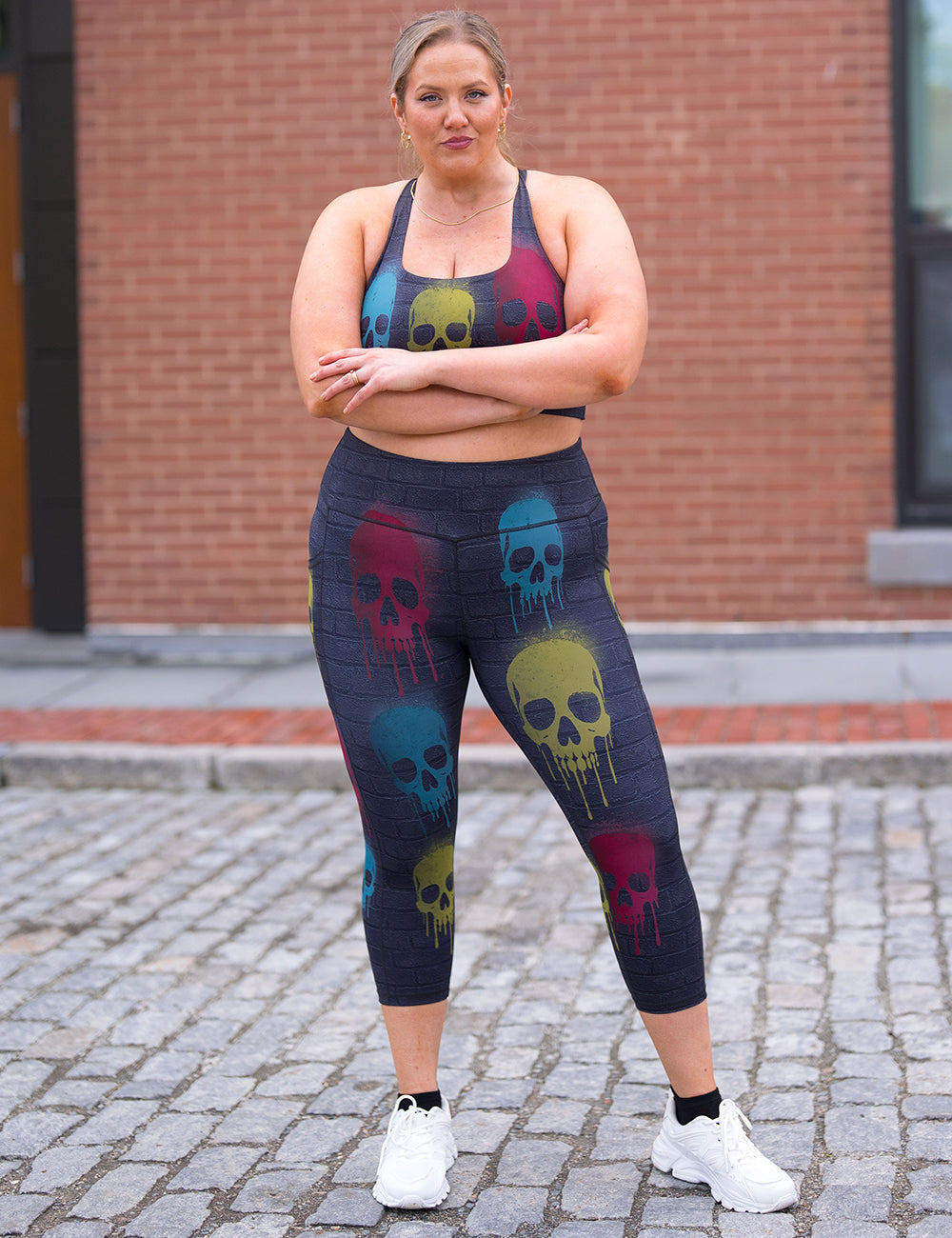 model wearing the black brick pattern capri leggings with spray painted yellow, blue, and red skulls all over