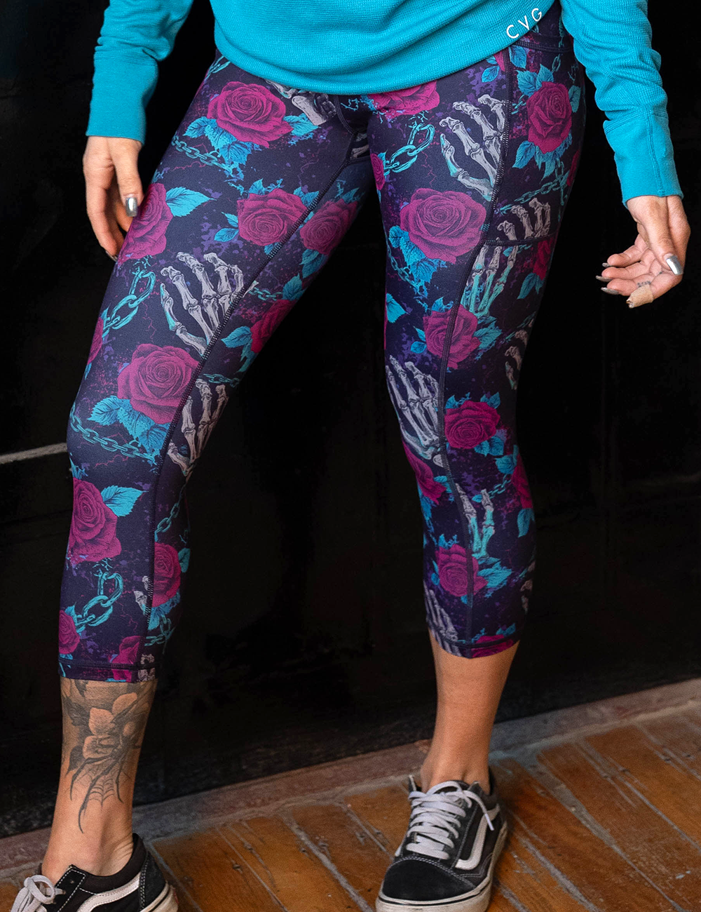 model wearing roses and skeleton hands connected by chain links pattern capri leggings against a rustic wood floor backdrop