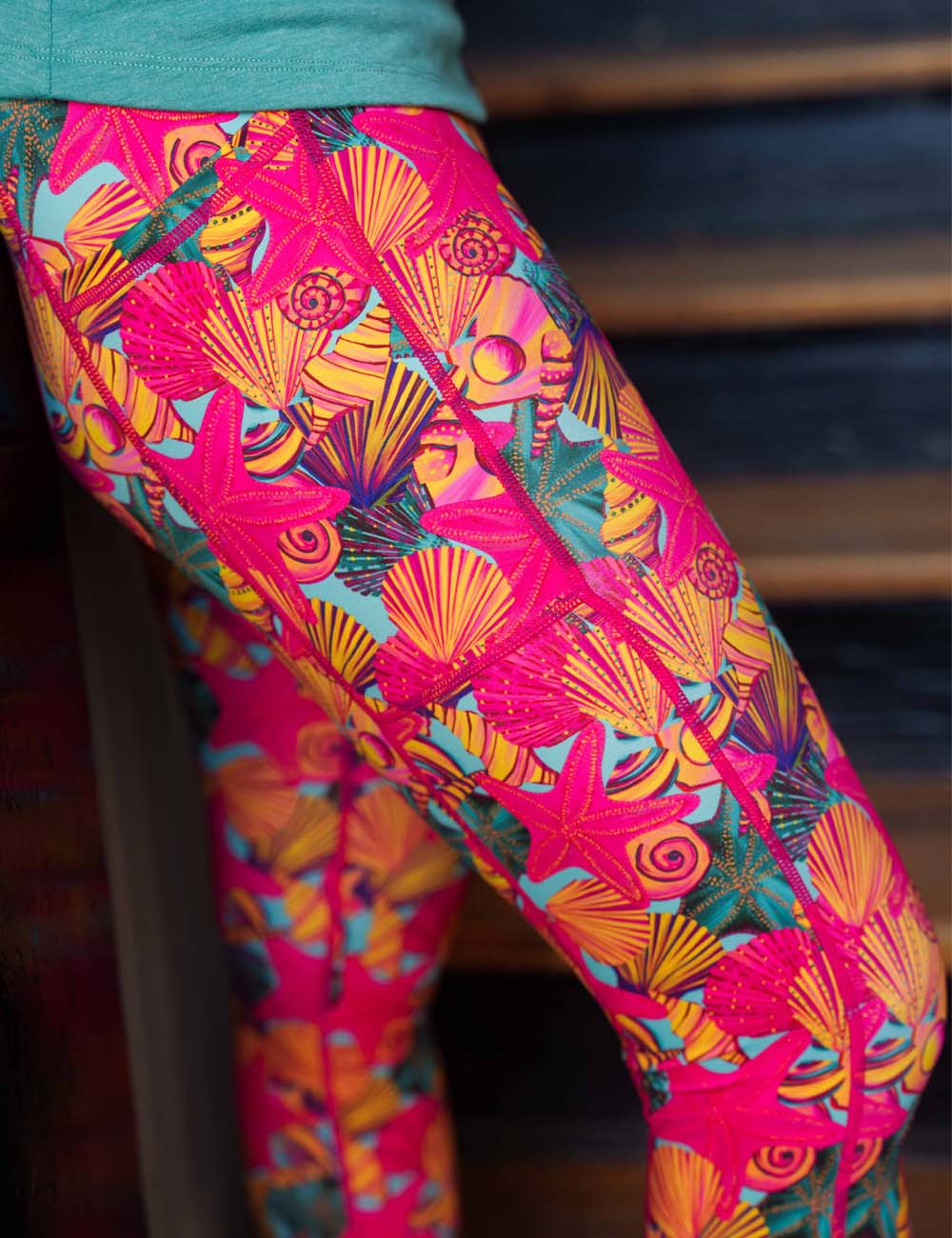 model wearing the full length red starfish with a yellow and blue shell background leggings in a stairwell